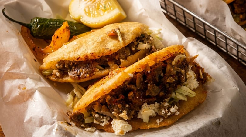 Two golden-fried gorditas filled with meat, cheese, and lettuce, served with a lemon wedge and pepper.