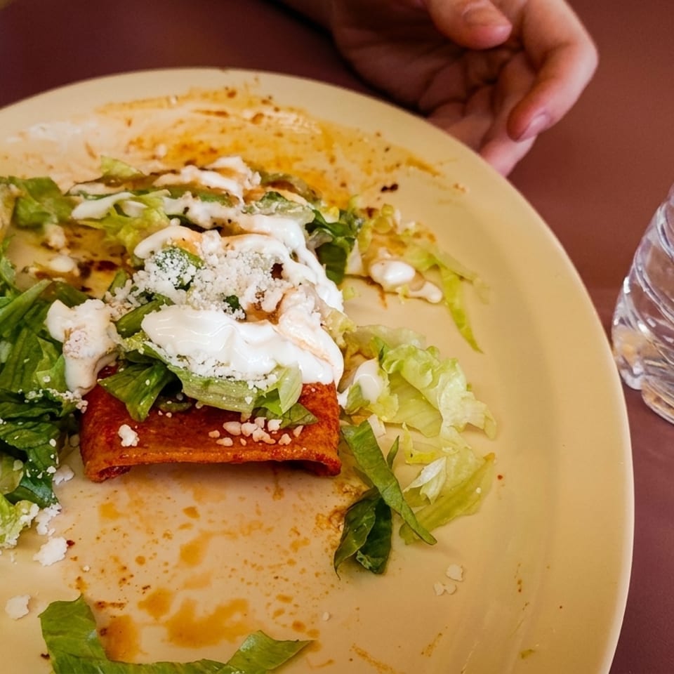 Partially eaten enchilada with lettuce, avocado, sour cream, and cheese on a yellow plate.